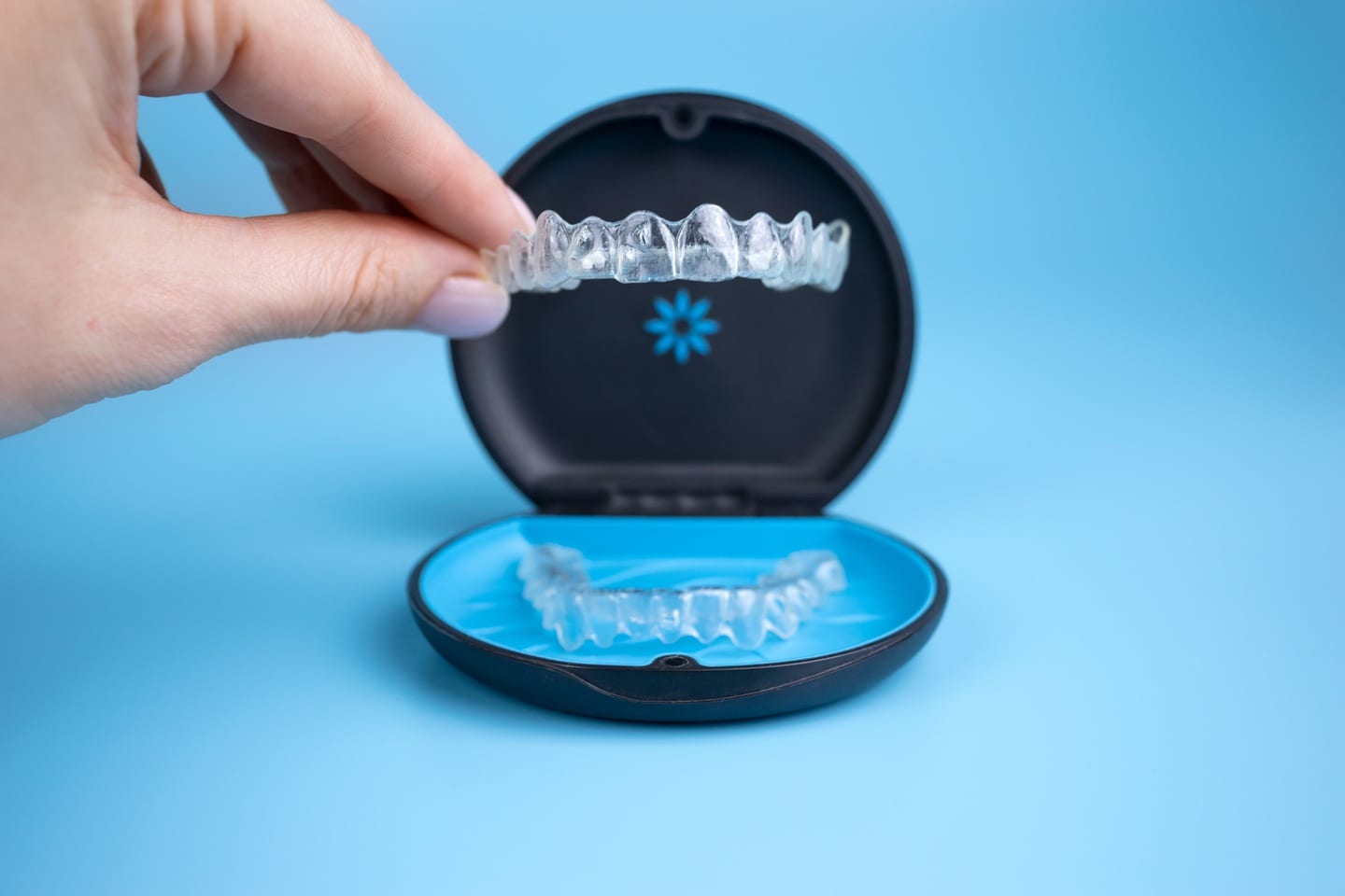 Hand holding an Invisalign clear aligner above its storage case